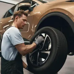 Mechanik w warsztacie wymienia oponę w samochodzie. To dobry moment, by pomyśleć, kiedy wymieniać opony na letnie.