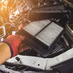 Wymiana filtrów w samochodzie. Ręka w rękawicy wyjmuje zużyty filtr powietrza z silnika.