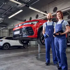 Dwóch mechaników w warsztacie przy czerwonym samochodzie na podnośniku. Sprawdzą, co obejmuje serwis samochodu, by zapewnić jego sprawność.