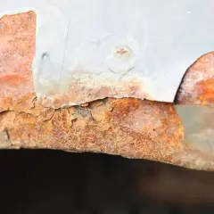 Widoczne bąble na lakierze samochodowym, pod którymi rozwija się rdza. Metalowy element jest mocno skorodowany, a lakier odpada.