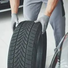 Mechanik w rękawiczkach trzyma oponę zimową, gotową do montażu. Sprawdzenie homologacji opon to klucz do bezpieczeństwa.