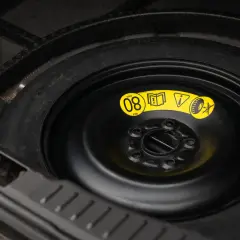 Koło dojazdowe w bagażniku samochodu, z żółtą naklejką informującą o maksymalnej prędkości 80 km/h.