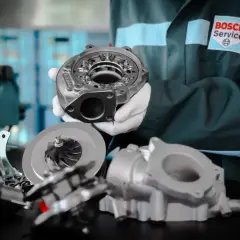Mechanik w białych rękawiczkach prezentuje części turbosprężarki, podkreślając jej precyzyjną geometrię.
