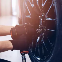 Mechanik w czarnych rękawiczkach używa klucza pneumatycznego do odkręcania śrub w błyszczącej feldze. Czy można wymienić jedną oponę? Tak, to właśnie się dzieje.