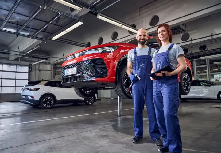 Dwóch mechaników w warsztacie przy czerwonym samochodzie na podnośniku. Sprawdzą, co obejmuje serwis samochodu, by zapewnić jego sprawność.