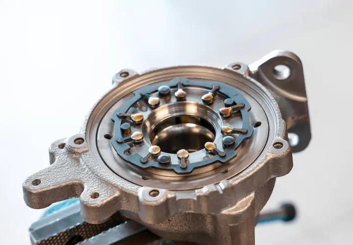 Metalowa obudowa turbosprężarki ze zmienną geometrią, z widocznym mechanizmem łopatek i elementami mocującymi.