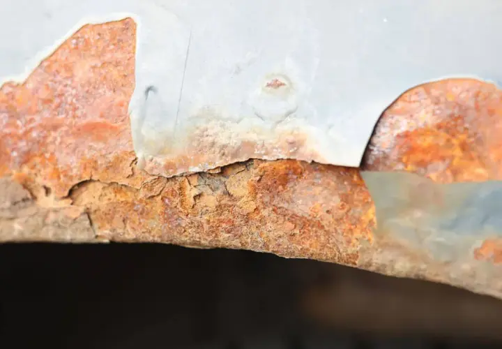 Widoczne bąble na lakierze samochodowym, pod którymi rozwija się rdza. Metalowy element jest mocno skorodowany, a lakier odpada.