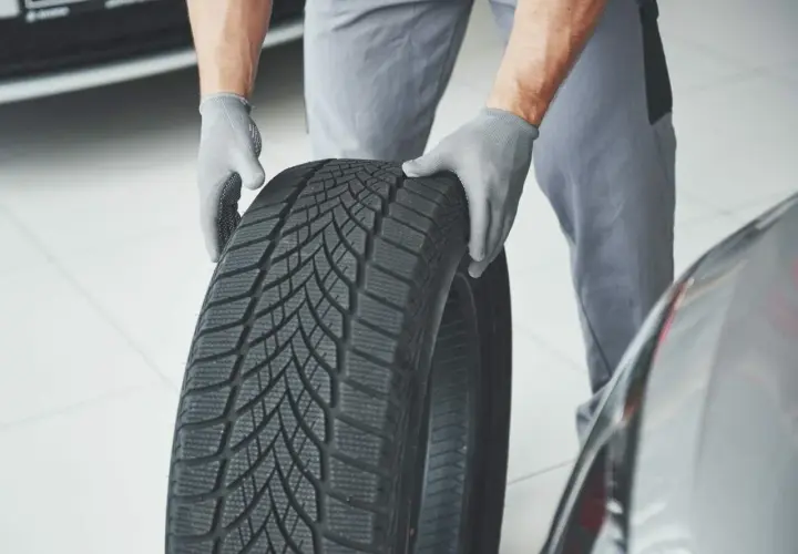 Mechanik w rękawiczkach trzyma oponę zimową, gotową do montażu. Sprawdzenie homologacji opon to klucz do bezpieczeństwa.
