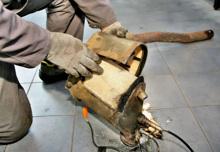 Mechanik w rękawiczkach rozkłada zapchany filtr DPF, przygotowując go do wypalania.