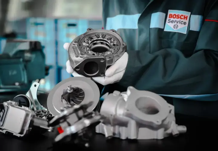 Mechanik w białych rękawiczkach prezentuje części turbosprężarki, podkreślając jej precyzyjną geometrię.
