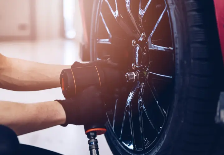 Mechanik w czarnych rękawiczkach używa klucza pneumatycznego do odkręcania śrub w błyszczącej feldze. Czy można wymienić jedną oponę? Tak, to właśnie się dzieje.
