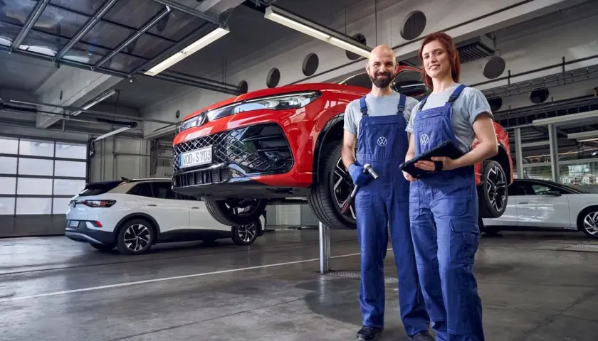 Dwóch mechaników w warsztacie przy czerwonym samochodzie na podnośniku. Sprawdzą, co obejmuje serwis samochodu, by zapewnić jego sprawność.