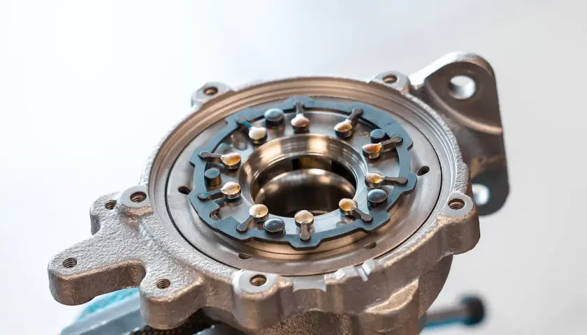 Metalowa obudowa turbosprężarki ze zmienną geometrią, z widocznym mechanizmem łopatek i elementami mocującymi.