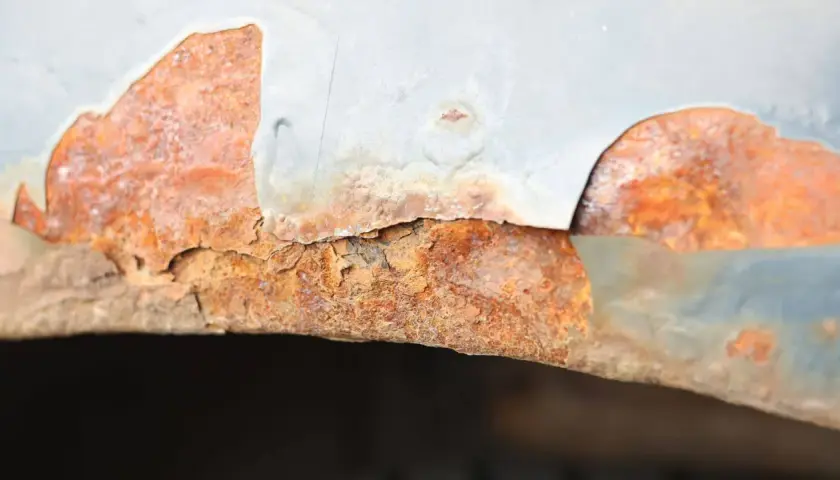 Widoczne bąble na lakierze samochodowym, pod którymi rozwija się rdza. Metalowy element jest mocno skorodowany, a lakier odpada.