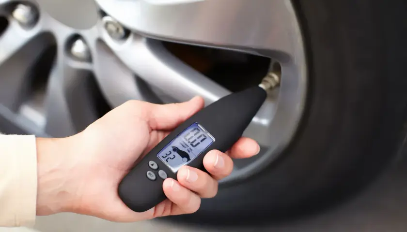 Dłoń trzyma miernik ciśnienia, który pokazuje 0.0 PSI. Wygląda na to, że uszkodzony czujnik ciśnienia w oponach uniemożliwia odczyt.
