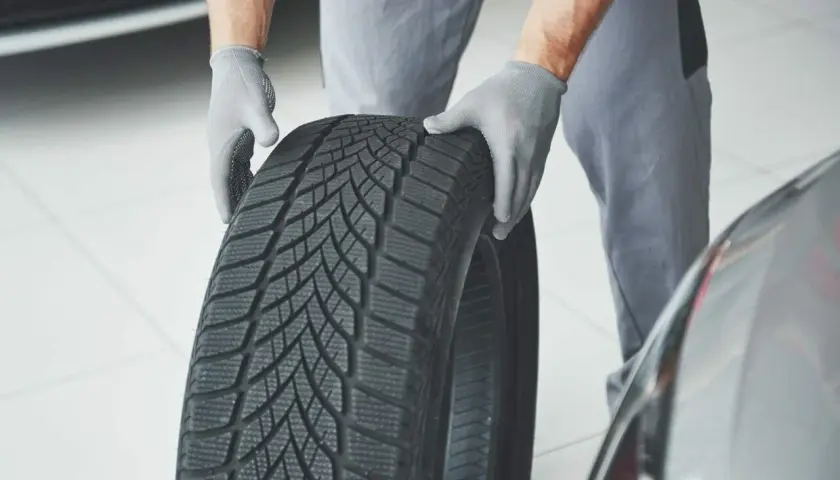 Mechanik w rękawiczkach trzyma oponę zimową, gotową do montażu. Sprawdzenie homologacji opon to klucz do bezpieczeństwa.