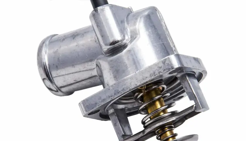 Metalowy termostat samochodowy z widocznym mechanizmem sprężynowym. Odpowiada za regulację temperatury silnika, a jego żywotność zależy od warunków pracy.