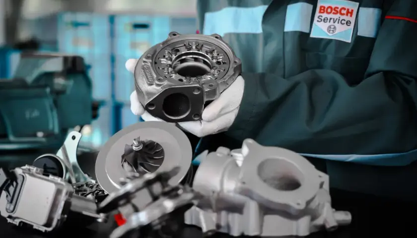 Mechanik w białych rękawiczkach prezentuje części turbosprężarki, podkreślając jej precyzyjną geometrię.
