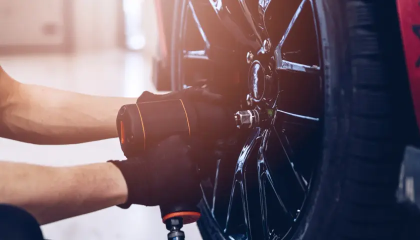 Mechanik w czarnych rękawiczkach używa klucza pneumatycznego do odkręcania śrub w błyszczącej feldze. Czy można wymienić jedną oponę? Tak, to właśnie się dzieje.