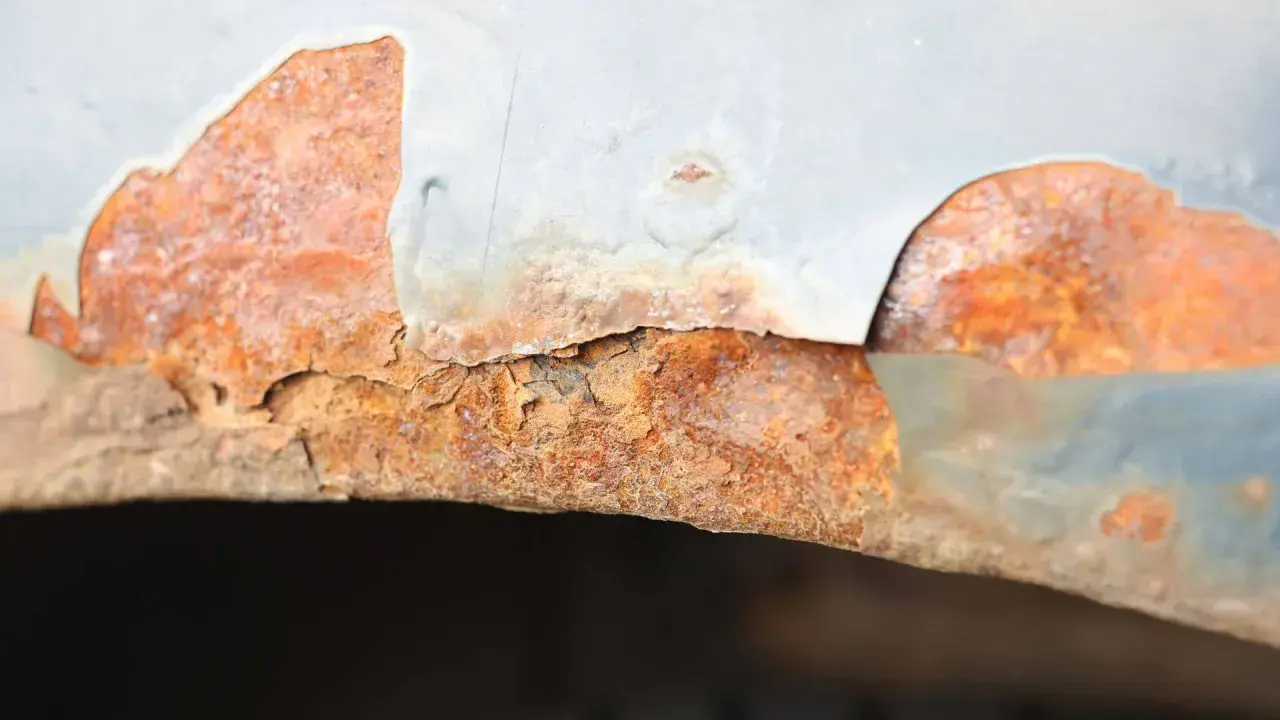 Widoczne bąble na lakierze samochodowym, pod którymi rozwija się rdza. Metalowy element jest mocno skorodowany, a lakier odpada.
