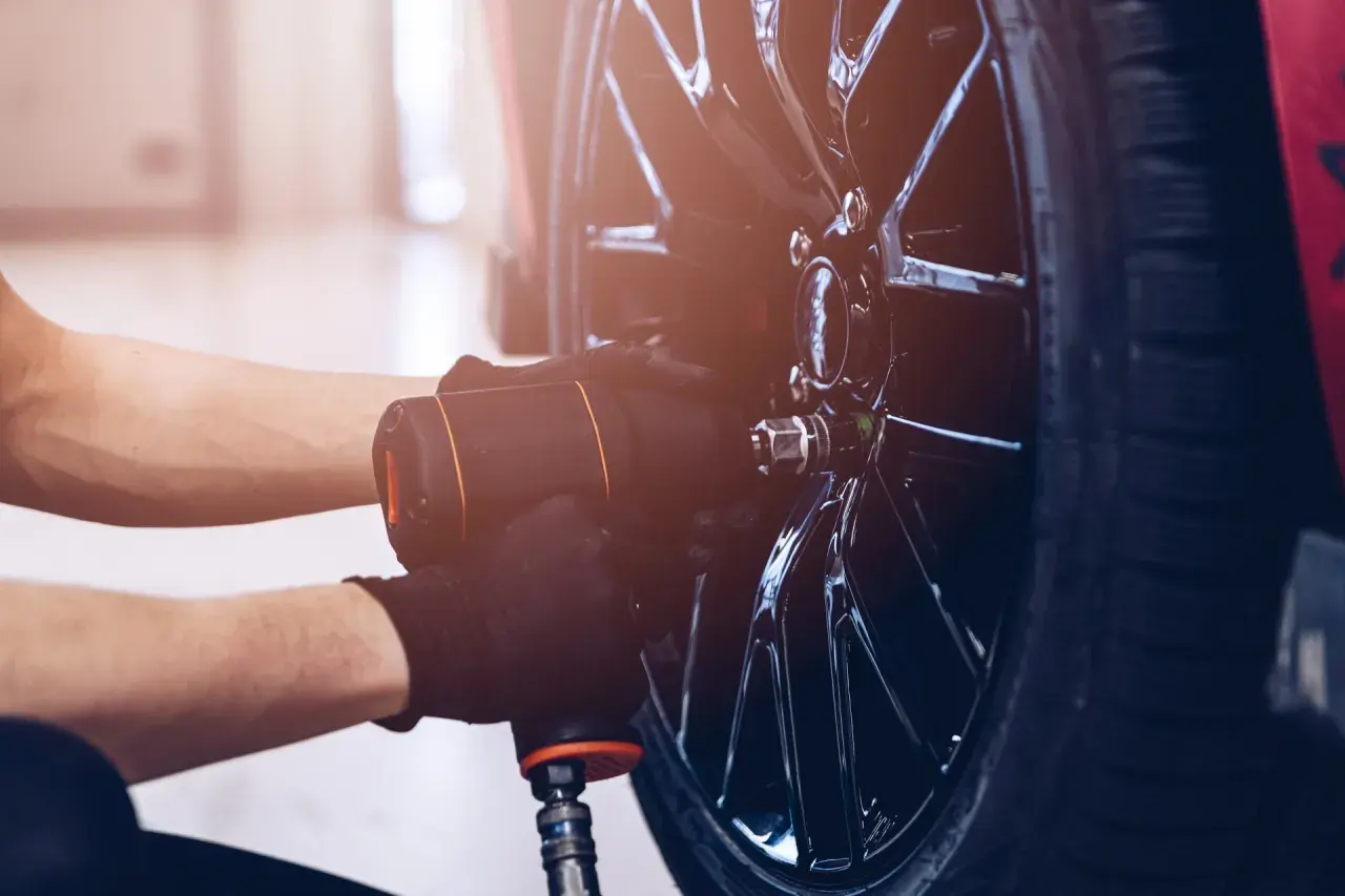 Mechanik w czarnych rękawiczkach używa klucza pneumatycznego do odkręcania śrub w błyszczącej feldze. Czy można wymienić jedną oponę? Tak, to właśnie się dzieje.