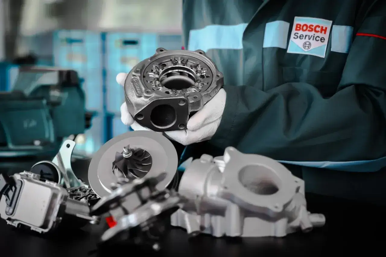 Mechanik w białych rękawiczkach prezentuje części turbosprężarki, podkreślając jej precyzyjną geometrię.