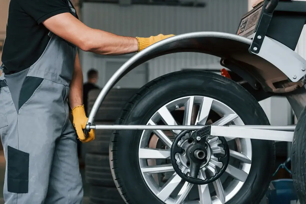 Mechanik w żółtych rękawiczkach ustawia koło z felgami nieprzelotowymi na wyważarce.