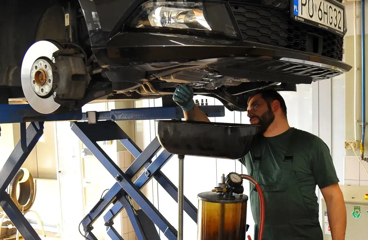 Mechanik wymienia olej w samochodzie, pokazując, co zrobić ze zużytym olejem.