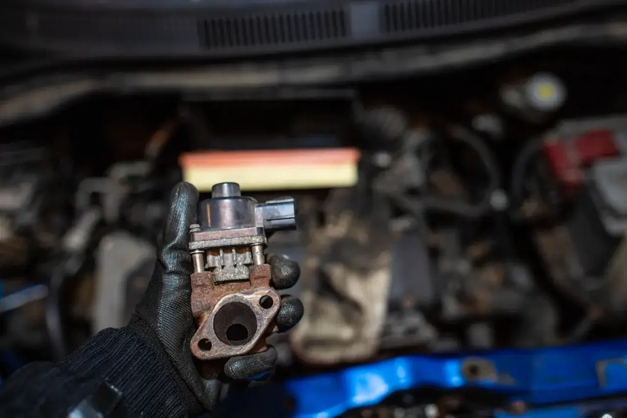 Zardzewiały zaw&oacute;r EGR w dłoni mechanika. Pokazuje, jak działa zaw&oacute;r EGR, recyrkulując spaliny.