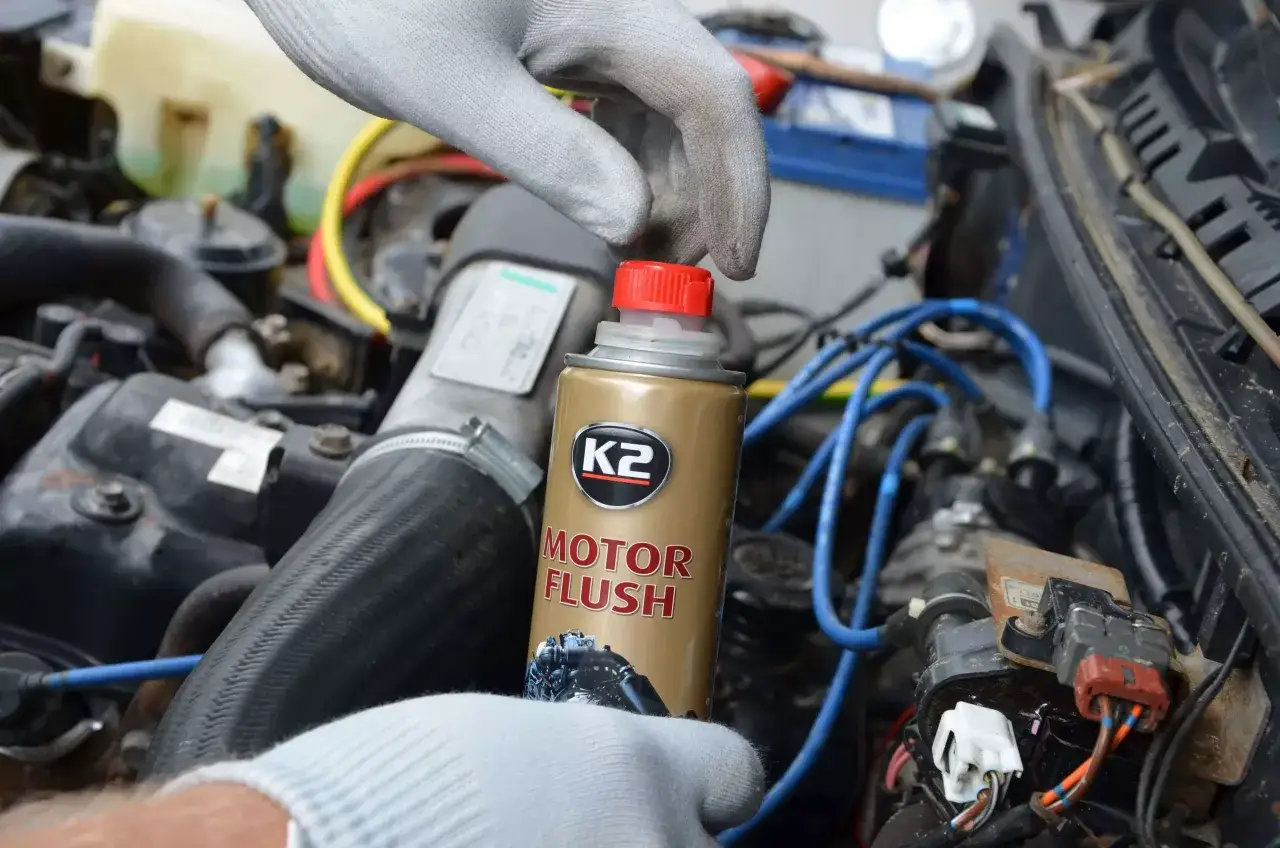Ręka w rękawiczce trzyma puszkę K2 Motor Flush, przygotowując się do płukania silnika.