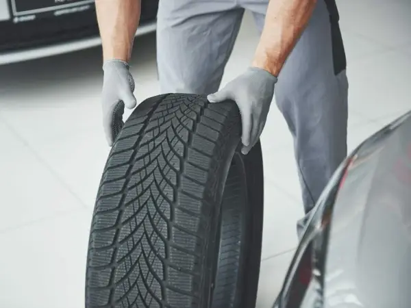Mechanik w rękawiczkach trzyma oponę zimową, gotową do montażu. Sprawdzenie homologacji opon to klucz do bezpieczeństwa.